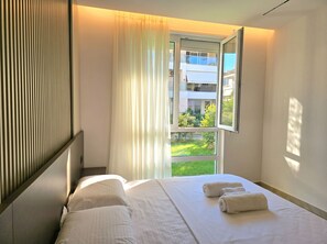 A hotel room with a bed, a window with curtains, and a view of greenery outside. - Relax Apartment By The Sea (Gjiri Lalzit)
