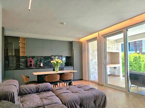 A modern kitchen with a dining area, a sofa, and a sliding glass door leading to a balcony. - Relax Apartment By The Sea (Gjiri Lalzit)