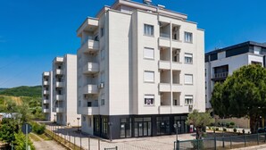 Edifício residencial com vários andares, varandas, entrada pavimentada e céu claro.