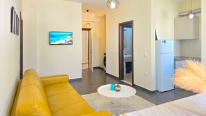 Uma sala moderna com um sofá amarelo, uma televisão de tela plana e um espaço de refeições com uma mesa pequena e cadeiras.