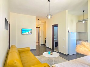 Ein modernes Wohnzimmer mit einem gelben Sofa, einem Flachbildfernseher und einer Essecke mit einem kleinen Tisch und Stühlen.