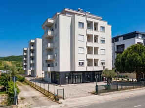 Ein mehrstöckiges Wohngebäude mit Balkonen, einem gepflasterten Eingangsbereich und blauem Himmel.