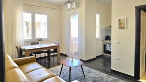 En moderne stue med en lædersofa, et spiseområde med bord og stole, og et køkken i baggrunden.