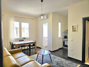 Ein modernes Wohnzimmer mit Ledersofa, Essbereich mit Tisch und Stühlen sowie Küche im Hintergrund.