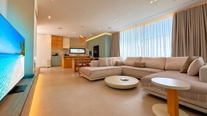 A modern living room with a large flat-screen TV, a sofa, a coffee table, and a kitchen in the background. - Superb Villa With Pool in San Pietro Resort (Gjiri Lalzit)