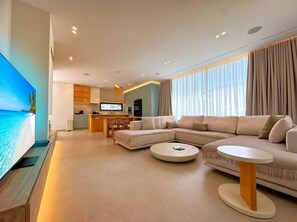 Ein modernes Wohnzimmer mit großem Flachbildfernseher, einer Couch, einem Couchtisch und einer Küche im Hintergrund.