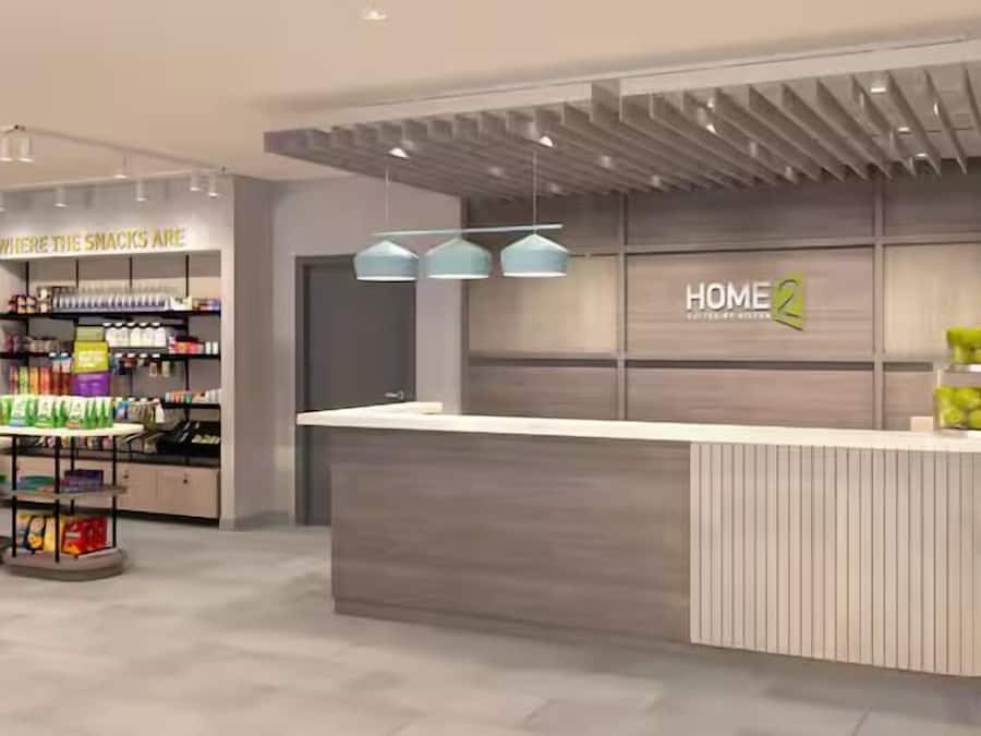A modern reception area with a counter, shelves stocked with snacks, and a sign that reads 'HOME 2'.