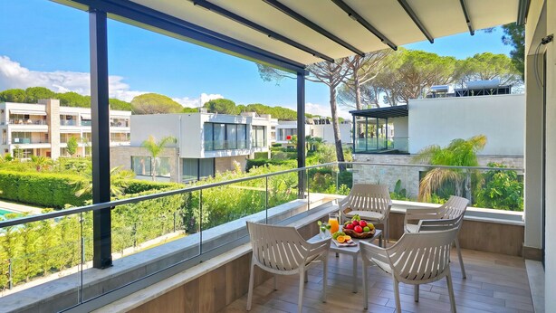 Varanda com mesa posta para dois, rodeada de cadeiras, com vista para área residencial com edifícios modernos e vegetação.