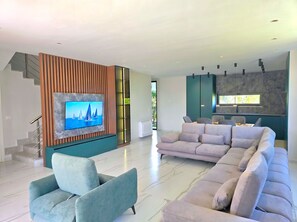 Ein modernes Wohnzimmer mit einem Ecksofa, einem Flachbildfernseher und einer Treppe.