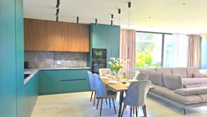 Uma cozinha moderna com forno embutido e micro-ondas, uma sala de jantar com mesa posta para dois e uma sala de estar com sofá.