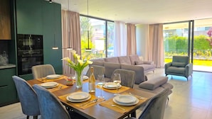 Uma zona de refeições moderna com mesa de madeira posta para quatro pessoas, forno embutido e vista para o exterior.