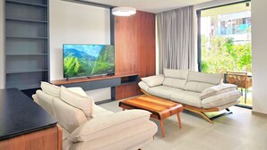 A modern living room with a flat-screen TV, a sofa, a coffee table, and a view of greenery outside. - Seaside Premium Villa (Gjiri Lalzit)