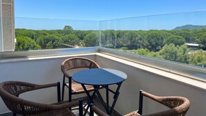 En balkon med fletstole og et bord, med udsigt over et skovlandskab.