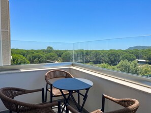 Ein Balkon mit Korbstühlen und einem Tisch, mit Blick auf eine bewaldete Landschaft.