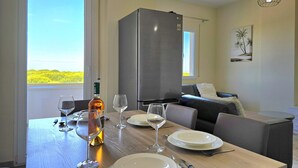 En spiseplads med et bord dækket til fire personer, en vinflaske og udsigt til grøn vegetation udenfor.