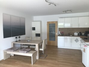 Eine moderne Küche mit weißen Schränken, ein Essbereich mit Tisch und Stühlen sowie ein großes Kunstwerk an der Wand.