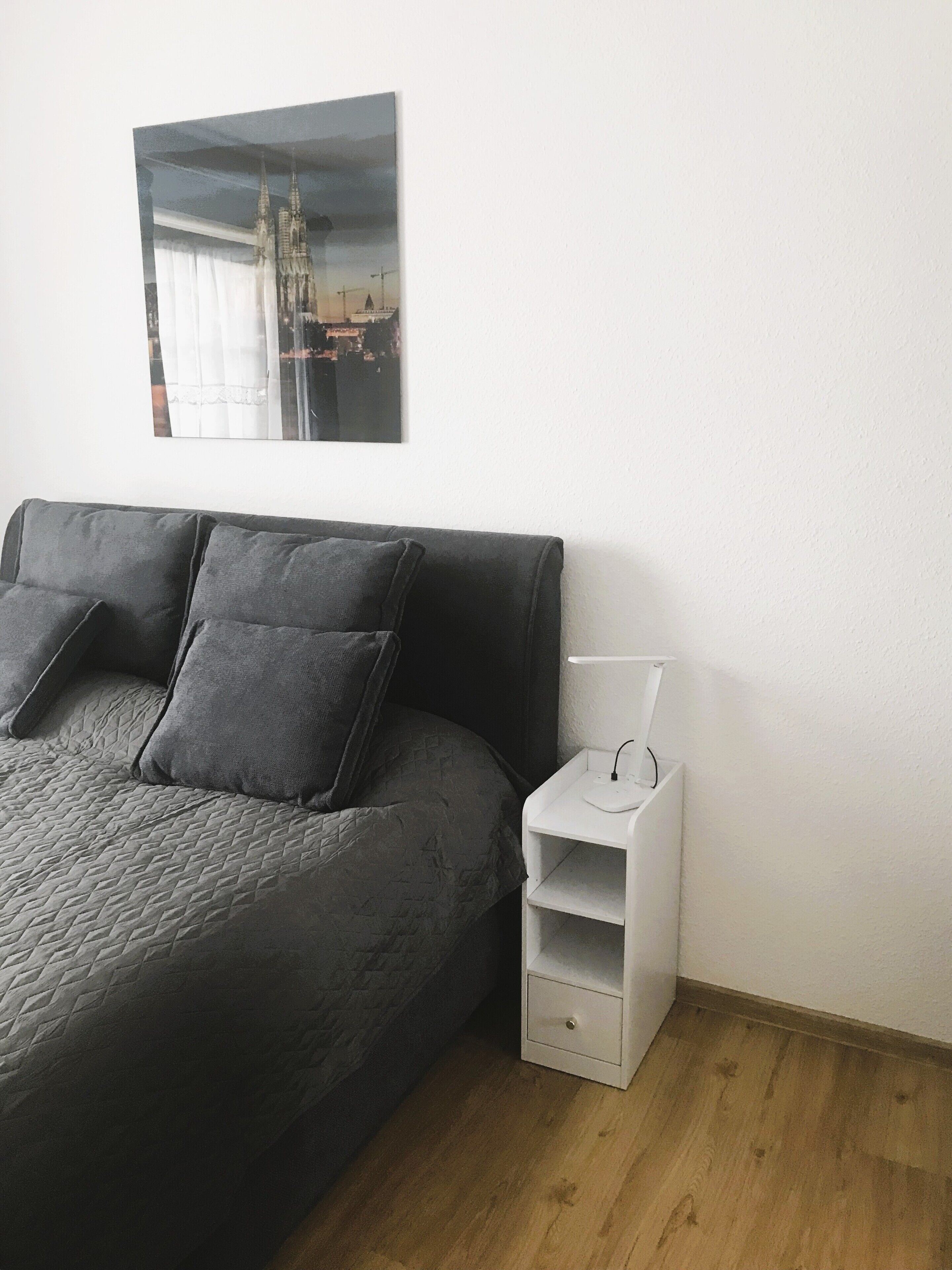 Una camera da letto moderna con un letto, cuscini, un comodino con una lampada e un quadro incorniciato appeso al muro.