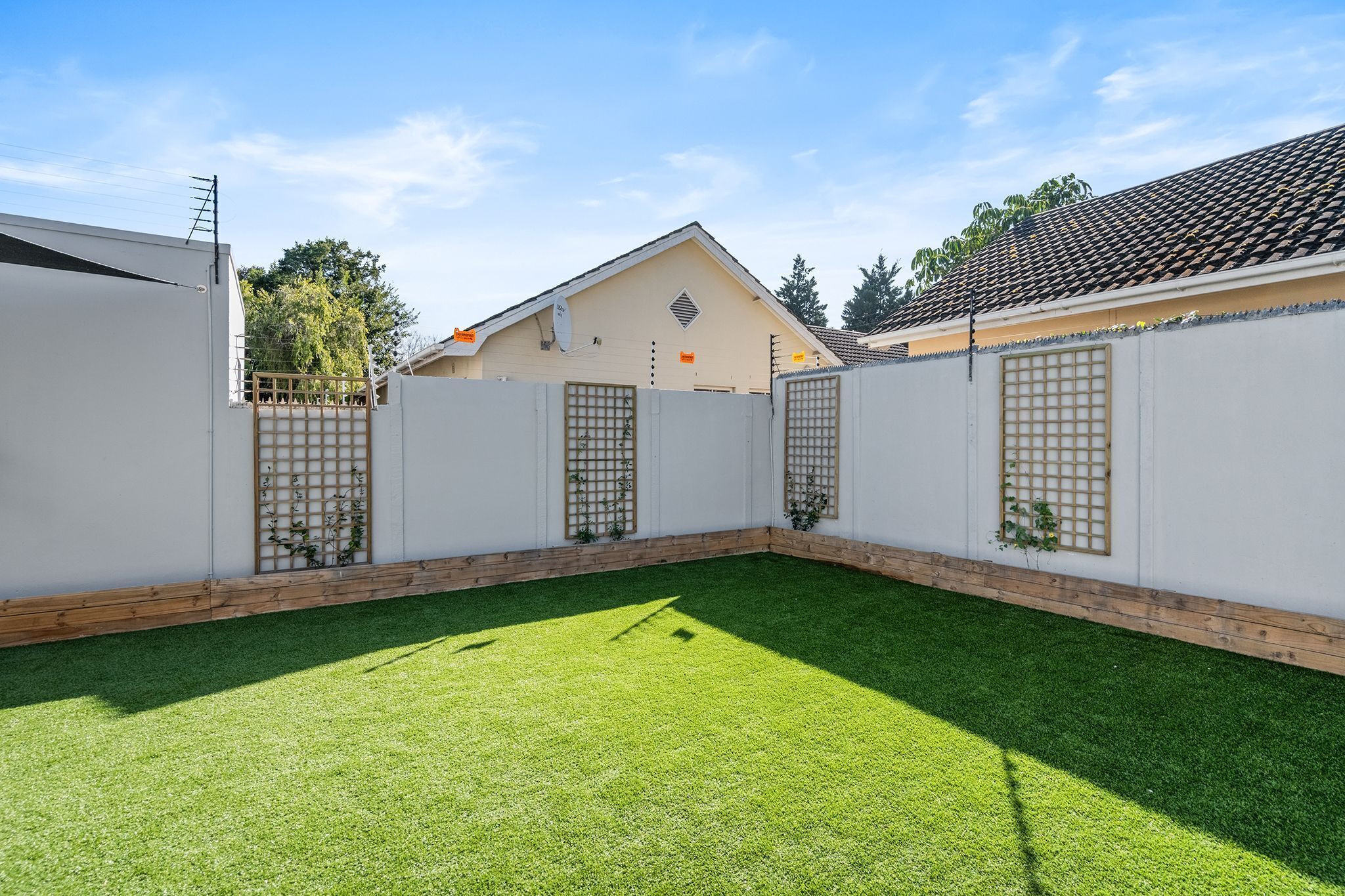 Ein eingezäunter Garten mit Kunstgrasanlage, einem Holzzaun und einem Gebäude mit Ziegeldach.