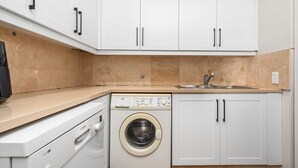 A compact kitchen with a washing machine, a sink, and white cabinets. - Sangrove Residence (Cape Town)
