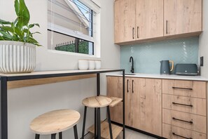 A modern kitchen with wooden cabinets, a black countertop, and a window with a view of greenery. - Sangrove Residence (Cape Town)