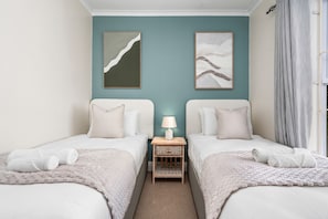 Une chambre double avec deux lits, une table de chevet avec une lampe et des œuvres d’art abstraites accrochées au mur.