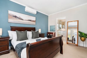 A bedroom with a wooden bed, a painting on the wall, a mirror, and a potted plant.