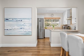A modern kitchen with white cabinets, a stainless steel refrigerator, and a dining area with a white table and chairs.