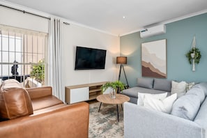 A modern living room with a sofa, armchair, TV, and a small table with a plant.