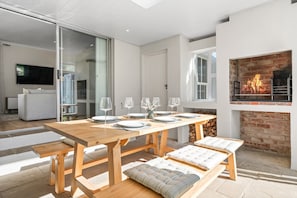 A modern dining area with a wooden table set for four, benches with cushions, a fireplace, and a television in the background.