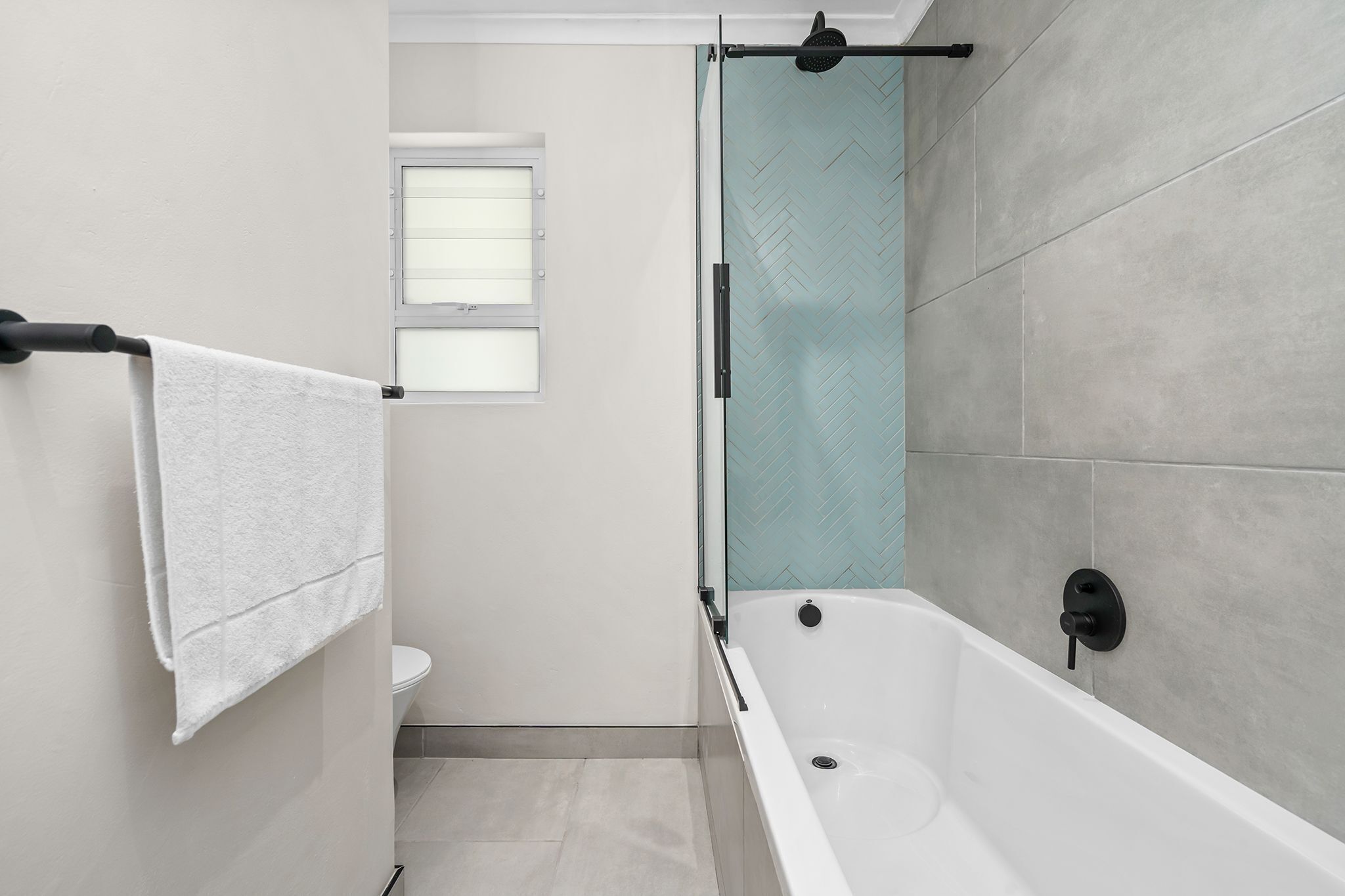 Ein Badezimmer mit einer Badewanne, einem Handtuchhalter, einer Toilette und einem Fenster.
