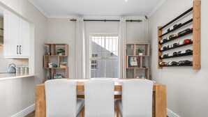A dining area with a wooden table, three chairs, a white curtain, and a wine rack on the wall. - Sangrove Residence (Cape Town)