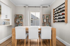 A dining area with a wooden table, three chairs, a white curtain, and a wine rack on the wall. - Sangrove Residence (Cape Town)