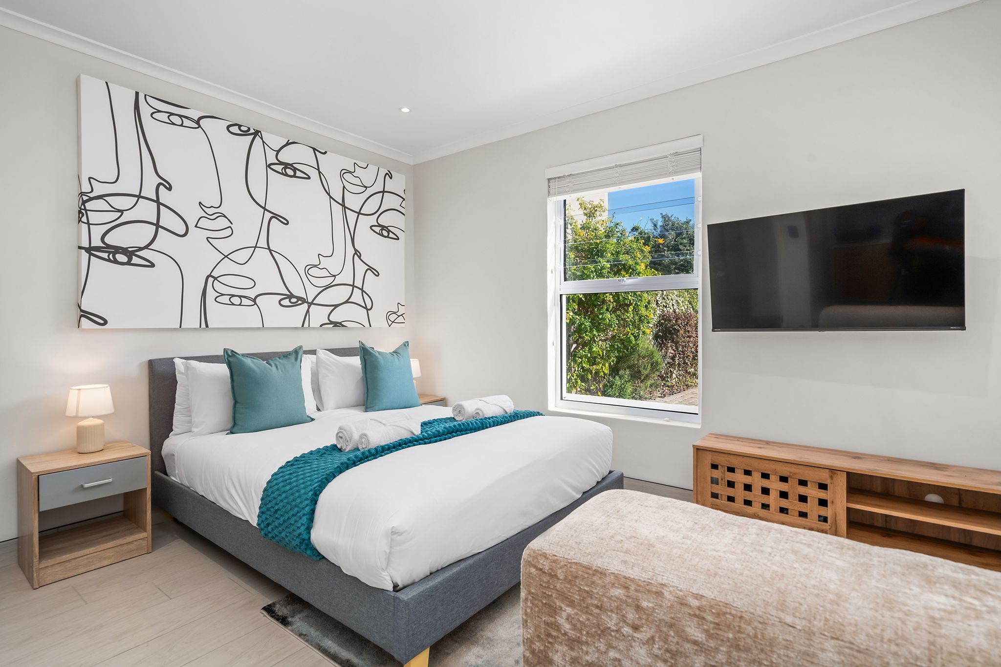 A modern bedroom with a bed, nightstand, TV, and artwork.