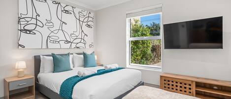 A modern bedroom with a bed, nightstand, TV, and artwork.