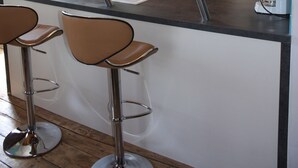Een keuken met een centraal eiland, barkrukken, een koffieapparaat en houten kasten.
