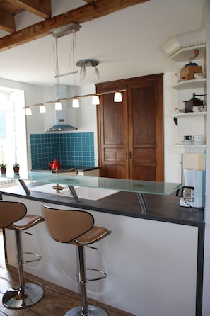 A kitchen with a central island, bar stools, a coffee machine, and wooden cabinets. - Le Jardin aux Lilas – Private Pool, Renovated House in Lot Valley (Cadrieu)
