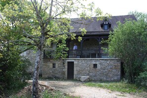 A stone building with a balcony, surrounded by trees and a gravel path. - Le Jardin aux Lilas – Private Pool, Renovated House in Lot Valley (Cadrieu)