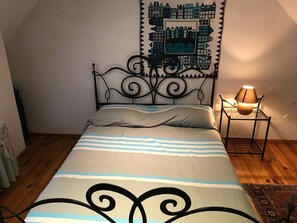 A bedroom with a bed, a wall tapestry, a bedside lamp, and a wooden floor. - La Bergerie – Private Pool (Cadrieu)