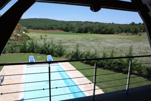 A view of a swimming pool with two lounge chairs, surrounded by a metal railing, with a grassy area and trees in the background. - La Bergerie – Private Pool (Cadrieu)