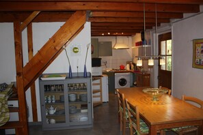 A kitchen with a wooden table, a washing machine, and a cabinet with dishes. - La Bergerie – Private Pool (Cadrieu)
