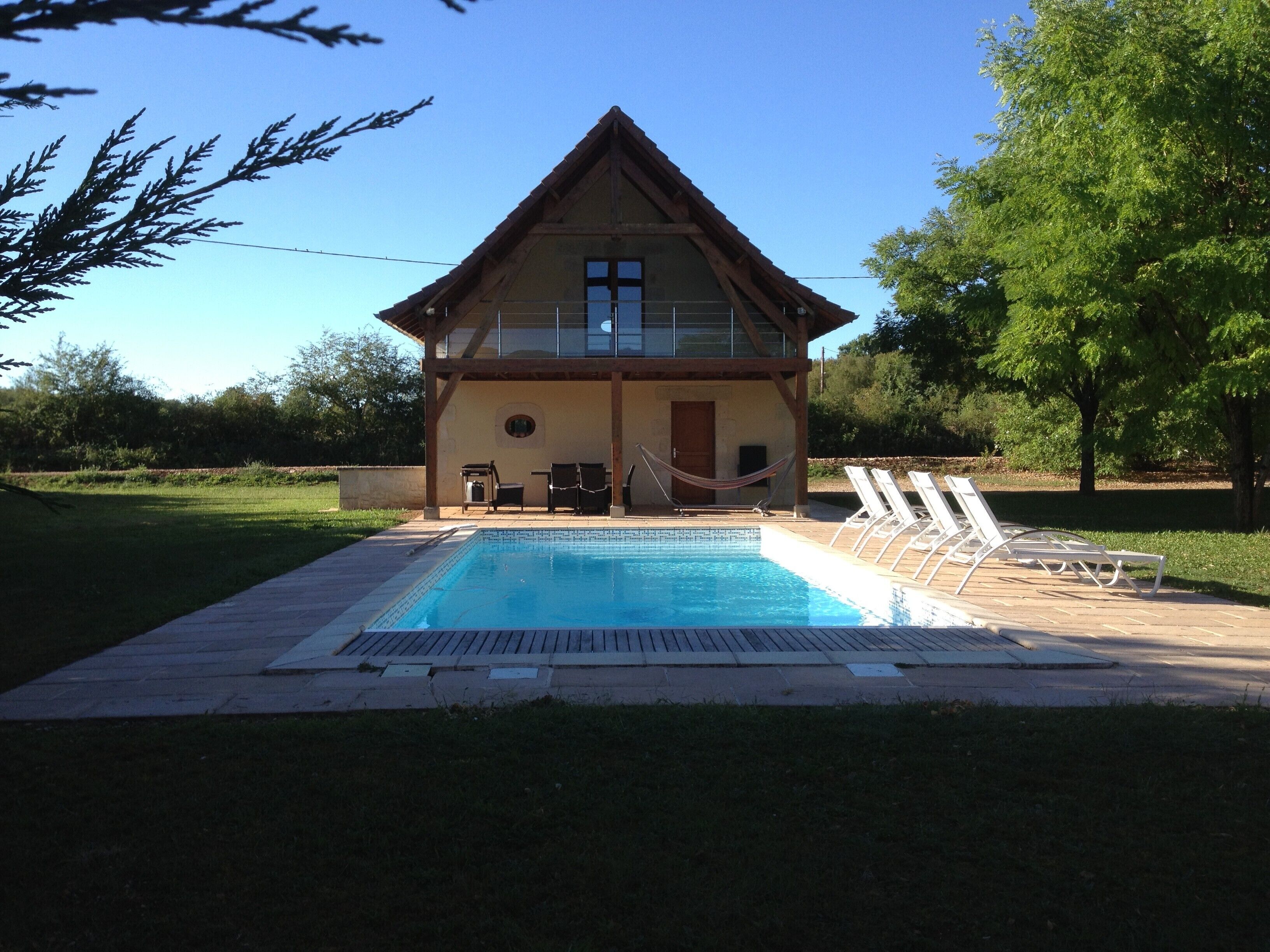 A two-story building with a swimming pool, lounge chairs, and a hammock.