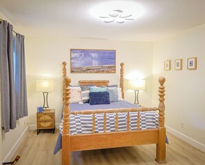 Ein Bett mit Baldachin, ein Kopfteil, zwei Nachttische, eine Wandleuchte, ein Gemälde und ein Fenster mit Vorhängen.
