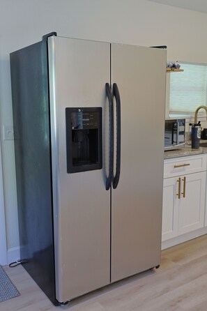 A stainless steel refrigerator with a built-in water dispenser, a microwave, and a sink area. - Blue Jay Bungalow (Safety Harbor)