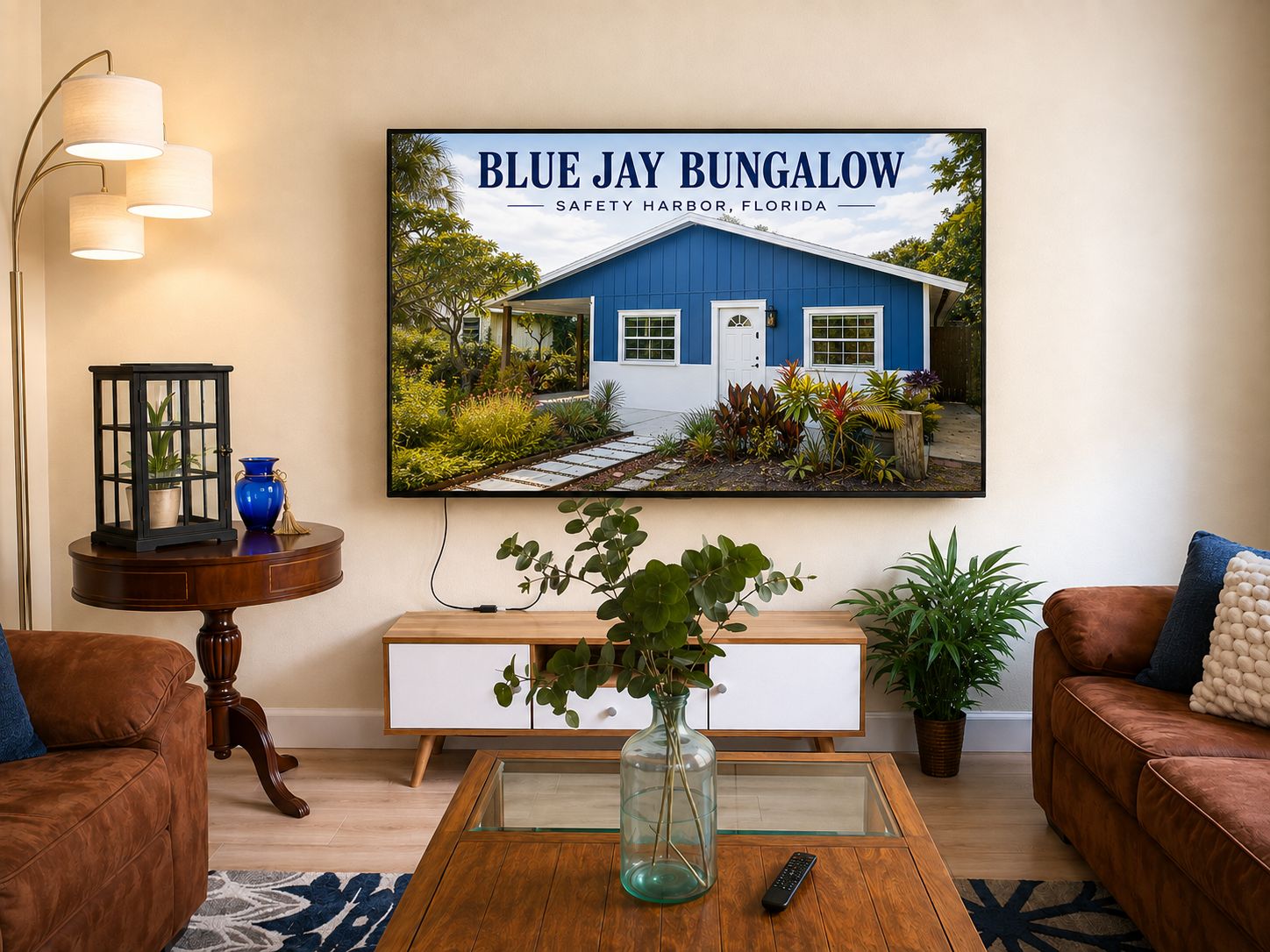 A living room with a large framed picture of a bungalow, a wooden coffee table, a brown leather sofa, a white console table, and a floor lamp.