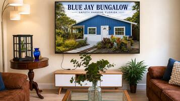 A living room with a large framed picture of a bungalow, a wooden coffee table, a brown leather sofa, a white console table, and a floor lamp.