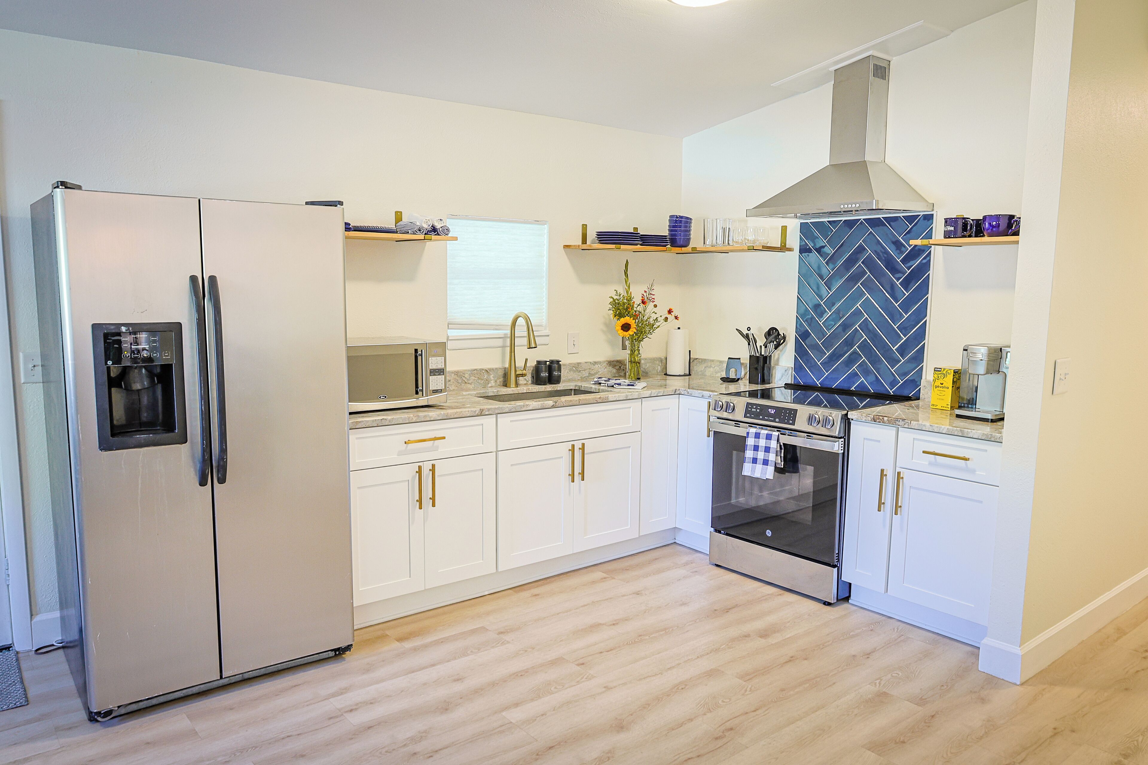 Una cocina moderna con gabinetes blancos, un refrigerador de acero inoxidable, horno empotrado y una salpicadera con estampado de espiga.