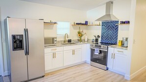 Eine moderne Küche mit weißen Schränken, einem Edelstahlkühlschrank, einem eingebauten Backofen und einer Rückwand mit Fischgrätmuster.