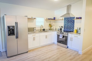 Eine moderne Küche mit weißen Schränken, einem Edelstahlkühlschrank, einem eingebauten Backofen und einer Rückwand mit Fischgrätmuster.