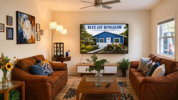 A living room with two brown leather sofas, a coffee table, a TV mounted on the wall, and a framed picture of a bungalow.