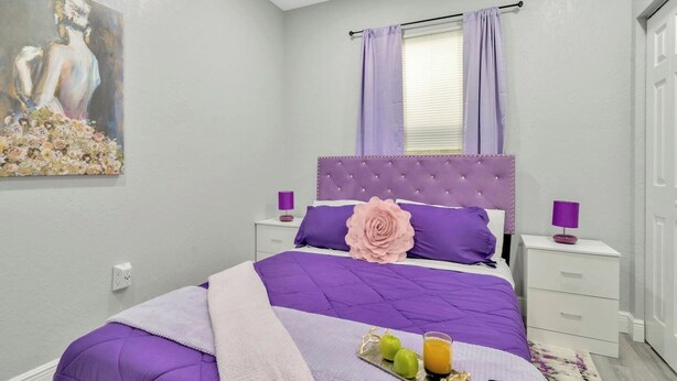 A bedroom with a bed, nightstands, a window with curtains, a painting on the wall, and a tray with apples and juice. - 2 Bed Oasis 10 Minutes to Downtown (tampa)